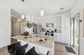A modern kitchen with a granite countertop and black chairs.